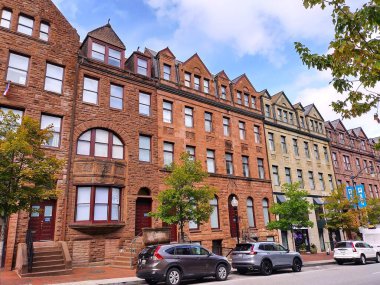 Baltimore, Maryland, USA  September 17, 2024: View of beautiful old brick townhomes in citycenter of Baltimore, MD with gable roofs. Cars parking on the street. Trees are planted on sidewalk.
