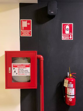 Lima, Peru - 24 Mayıs 2025: Duvar, depolanmış yangın söndürücü ve kırmızı boyalı su borusuyla iç yangın hortumu. İspanyolca işaretler yangın durumunda nasıl kullanılacağı konusunda talimat verir. Dikey.