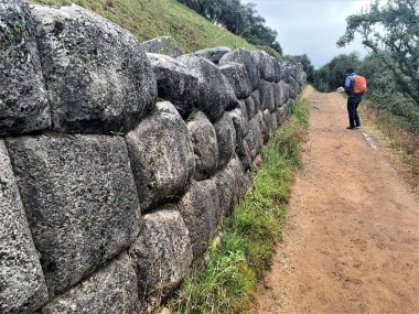 Tarihi İnka İmparatorluğu kalesi Sacsayhuaman 'ın (Saqsaywaman) ziyaretçisi kuru taş duvarın yanındaki toprak yolda yürüyor. Taş işçiliği, dağlık arazi, eğimli tepe, yürüyüş sırt çantası.