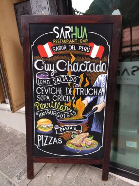 Aguas Calientes, Peru - 27 Mayıs 2025: Renkli çizimlerle süslenmiş karatahtaya yazılmış Peru yemeklerini kapatın. Tipik yemek olarak cuy (kobay). Güzel tasarım. Dikey resim