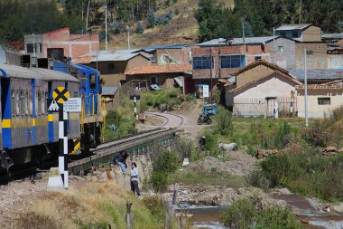 Cusco, Peru - 28 Mayıs 2025: Perurail tarafından işletilen Titicaca treni Kutsal Vadi 'den geçiyor. Lokomotif Urubamba nehri üzerinde köprüden geçiyor. Demiryolu kenarındaki insanlar.