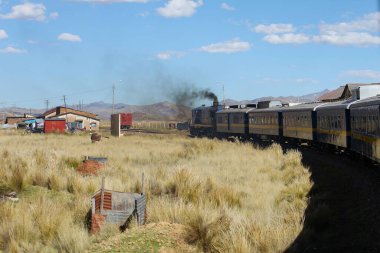 Puno, Peru - 28 Mayıs 2025: Titicaca treni Perurail tarafından And dağ sırtı ile etkileyici Altiplano arazisinde kullanıldı. Ferrocarril del Sur. Kalın dizel bulutlar yığından duman çıkıyor..