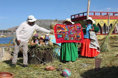 Puno, Peru - 29 Mayıs 2025: Tur rehberi Uros Yüzen Adası 'ndaki el yapımı nakışı açıklıyor. Tipik renkli sazlık teknesi demirlemiş. Titicaca Gölü 'ndeki Uros Adaları veya Uru Adaları.