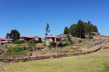 Taquile Adası, Puno, Peru - 29 Mayıs 2025: Titicaca Gölü 'ndeki taş duvarların arkasındaki yerleşim yerleri, plantasyonlar ve küçük tarlalar ile huzurlu bir yerleşim yeri. Tepedeki okaliptüs ağaçları.