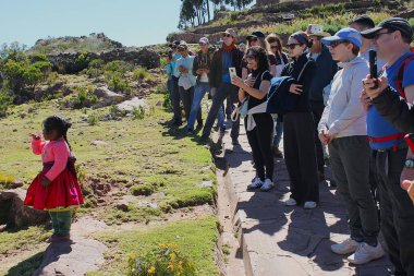 Isla Taquile, Puno, Peru - 29 Mayıs 2025: Geleneksel giysiler içinde, kendinden geçmiş turist topluluğu etrafını sarıp Titicaca Gölü 'ndeki bir adada fotoğraf çekiyor.. 