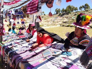 Isla Taquile, Puno, Peru - 29 Mayıs 2025: Geleneksel giysiler içindeki iş odaklı Taquileos, Titicaca Gölü 'ndeki bir adada el sanatları standında renkli dikiş işi sunuyor.