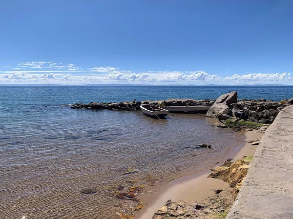 Taquile Adası, Puno, Peru: Puerto Huayllano rıhtımında Titicaca Gölü 'ne demir atmış bir kayık. Bulutlar büyük bir yükseliş nedeniyle alçaktan sarkmış görünüyor. Derin mavi su ve bulutsuz gökyüzü.