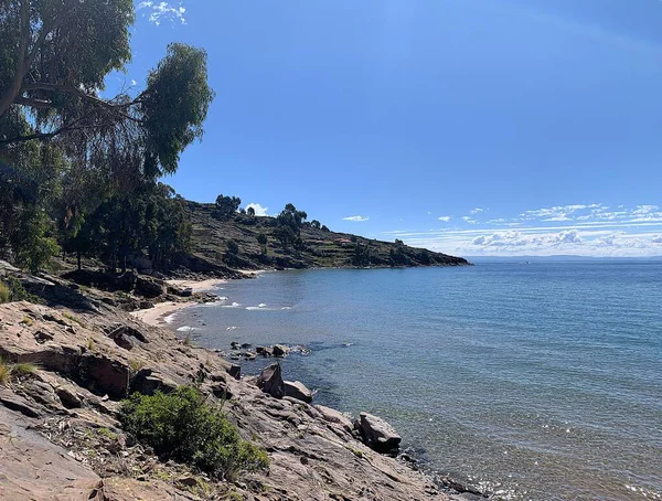 Taquile Adası, Puno, Peru: Titicaca Gölü 'nde Puerto Huayllano yakınlarındaki körfez ve plajlara panoramik manzara. Bulutlar büyük bir yükseliş nedeniyle alçaktan sarkmış görünüyor. Derin mavi su ve bulutsuz gökyüzü. 