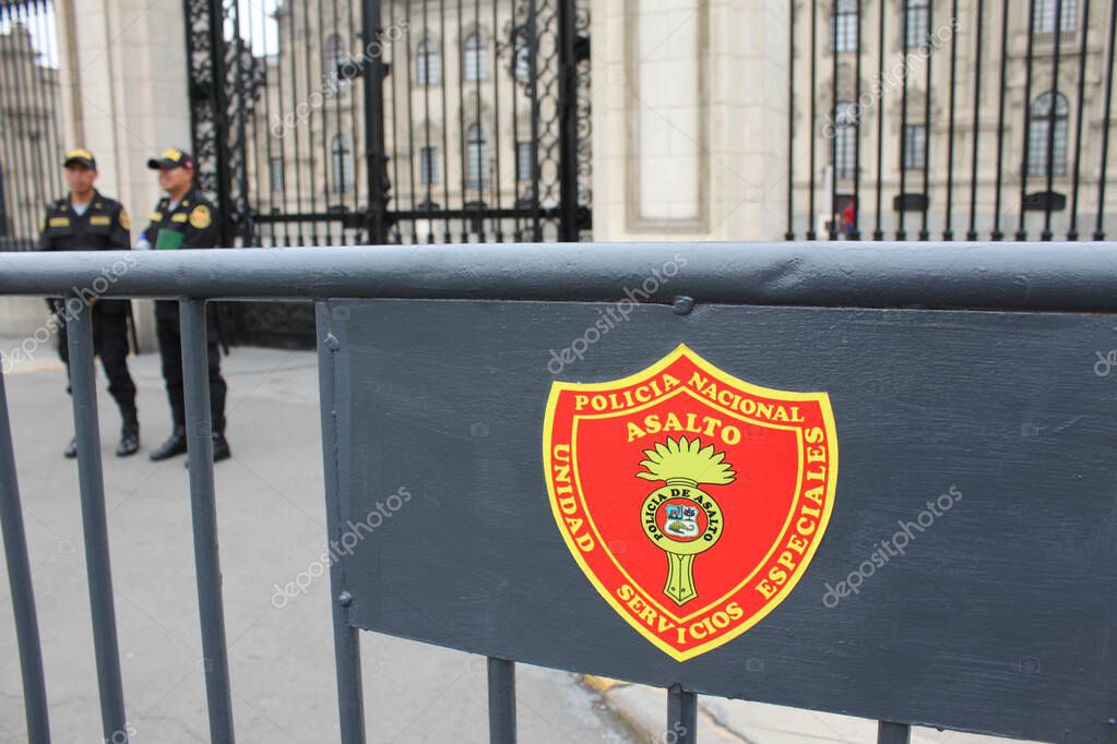 Lima, Peru - May 24, 2025: Coat of arms of National Police Assault Unit, Special Services Unit (Policia Nacional de Asalto, Unidad Servicios Especiales) on dark painted metal barrier. Officers present.