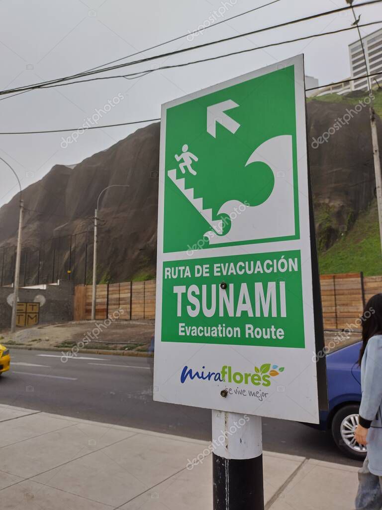 Miraflores, Lima, Peru - May 24, 2025: Green sign indicating escape route to stairs leading to higher terrain from beach. Spanish and English words: Evacuation route, Tsunami.