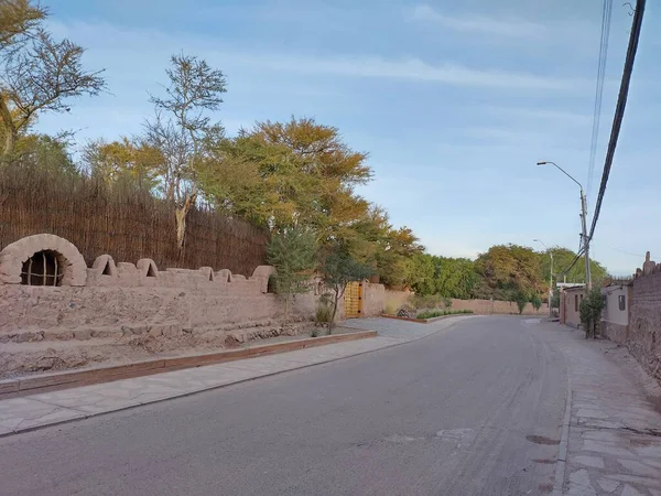 San Pedro de Atacama, El Loa, Antofagasta, Şili - Haziran 05, 2025: Tocopilla yolu şehir merkezinde kil duvarların üzerinde yeşil ağaç dalları asılı. Boş cadde, araç ya da yaya yok..