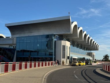 Otopeni, Romanya - 29 Ekim 2025: Geliş terminalinin cam cepheli ayırt edici binası. Giriş kapısının önünde kırmızı beyaz tırabzanlar, yolcular ve ziyaretçiler olan bir araç rampası..