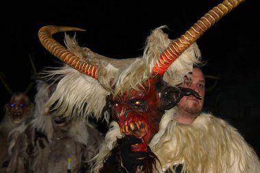 Gaenserndorf, Aşağı Avusturya - 28 Kasım 2025: Maskenin arkasındaki insan yüzü: Genç adam boynuzlu oğlak boynuzlarıyla korkunç Krampus kostümünü çıkardı. Perchtenlauf, Alp folklorik geleneği.