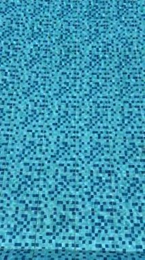 Yüzme havuzu zemininde mavi mozaik fayansların dikey döngü videosu. Titreyen dalgalarla ve soyut geometrik ışık yansımalarıyla hareket eden su yüzeyi. Turkuaz su arkaplanı tazeleniyor.