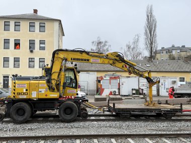 Gaenserndorf, Aşağı Avusturya - 10 Aralık 2025: Strabag markalı Sarı Liebherr 900 karayolu kazıcısı OeBB tren istasyonunda çakıl döşeme çalışması yapıyor.