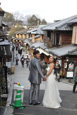Kyoto, Kansai, Japonya - 12 Şubat 2016: Geleneksel ahşap evleri olan tarihi Sannenzaka Ninenzaka 'da taş merdivenlerde el ele tutuşan yeni evli çift, gümüş takım elbise ve beyaz gelinlik. Dikey.