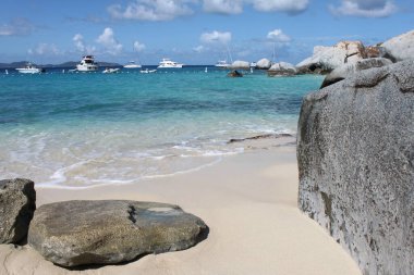 Virgin Gorda, Britanya Virgin Adaları - 25 Kasım 2016: Mavi gökyüzü altında turkuaz körfezde yüzen çok sayıda beyaz kayıkla Hamamlar 'da kumlu kıyı ve dokulu granit kayaların yakın görüntüsü.