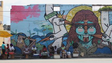 Cartagena, Bolivar, Kolombiya - 01 Aralık 2016: Getsemani ilçesinin yıkılmış duvarında kadın yüzü ve kuşların olduğu büyük renkli sokak resimleri önünde oturan yerel balık satıcıları.