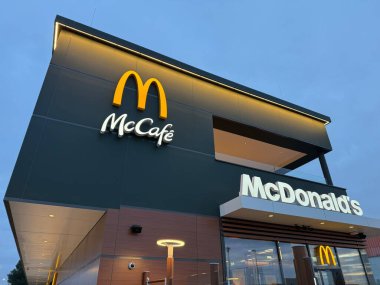 Gaenserndorf, Aşağı Avusturya - 08 Şubat 2026: Modern McDonald 's restoranının dış cephesi cam ve geceleri parlayan sarı M logosu. Küresel fast food şubesi mimarisi.