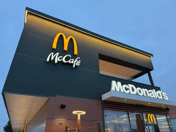 Gaenserndorf, Aşağı Avusturya - 08 Şubat 2026: Modern McDonald 's restoranının dış cephesi cam ve geceleri parlayan sarı M logosu. Küresel fast food şubesi mimarisi.