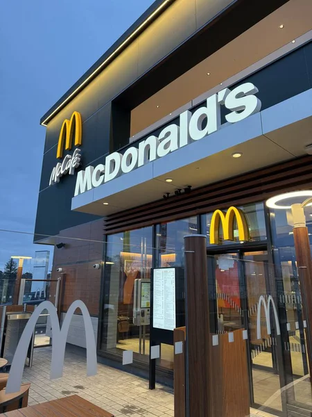 Gaenserndorf, Aşağı Avusturya - 08 Şubat 2026: Parlak tabelalı McDonald 's restoranı ve McCafe binasının geniş gece görüşü. Karanlık gökyüzü altında ticari fast food mimarisi. Dikey.