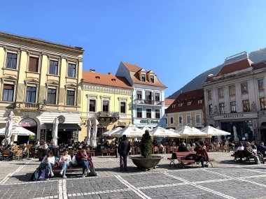 Brasov, Romanya - 23 Ekim 2025: Kronstadt 'taki Piaa Sfatului (Council Square) veya Transilvanya, Siebenbuergen' deki Brasso 'da yoğun açık hava kafeleri. İnsanlar eski kasabada sonbaharda güneşli bir günün tadını çıkarırlar. Doğu Avrupa 'da hareketli şehir merkezi.