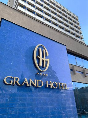 Targu Mures, Transilvanya, Romanya - 25 Ekim 2025: Mavi fayanslı duvardaki Grand Hotel logosunu kapatın. Annunciation Katedrali 'nin yansıması. Şehir merkezinde bir dönüm noktası. Güneşli bir gün. Dikey resim.