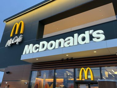 Gaenserndorf, Aşağı Avusturya - 08 Şubat 2026: Geceleri McDonald 's ve McCafe' nin ön manzarası. Küresel fast food restoranının modern cam ön cephesi. Parlak sarı işaretli..