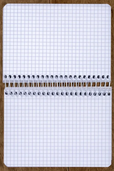 Açık boş spiral defter kare kağıt ile meşe masada bağlı.