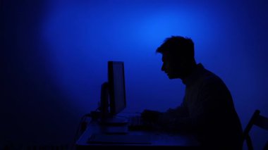 Karanlık bir odada, masasında oturan bir adamın silüeti. Bir bilgisayar ekranından gelen mavi ışıkla aydınlatılmış. Aşırı çalışmaktan oluşan stres, tükenmişlik ve yalnızlık kavramlarını temsil ediyor.