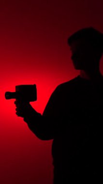 vertical video Silhouette of a person holding a retro film camera, capturing footage against a red background with a dramatic spotlight, representing concepts of filmmaking, nostalgia, and creativity