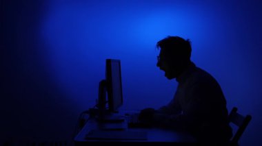 Bir bilgisayarın ofisinde çalışan esneyen bir adamın silüeti. Adam masasında uyumak istiyor. Fazla mesai. İş yerinde yorgunluk. Esneyen adam.