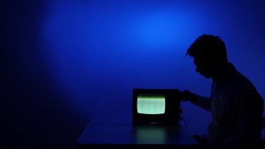 Eski bir eski televizyondan sinyal ayarlayan bir adamın silueti. Adam kanal değiştiriyor, eski televizyonun akort düğmelerini çeviriyor. Sinyal kaybı.