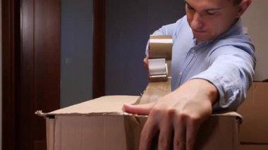 Adam karton bir nakliye kutusunu yapışkan bir bant kutusuyla koruyor, taşınmaya, teslimata ya da paket göndermeye hazırlanıyor, ambalaj, lojistik ve yer değiştirme kavramlarını vurguluyor.