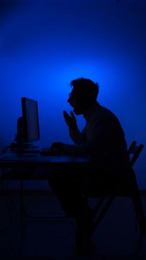 Bir bilgisayarın ofisinde çalışan esneyen bir adamın silüeti. Adam masasında uyumak istiyor. Fazla mesai. İş yerinde yorgunluk. Esneyen adam.