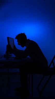 dikey video Mans siluet çığlık ve eller bir bilgisayar ekranında işaret, yoğun hayal kırıklığı, stres ve öfke ifade mavi ışık ile karanlık bir odada