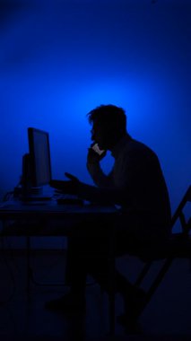 düşey video adam silueti bilgisayarda çalışıyor ve mavi ışık altında bir masada telefonla konuşuyor, siber güvenlik, ağ yönetimi, gece geç saatlere kadar çalışma ya da teknik destek gibi kavramları tasvir ediyor.