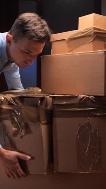 Dikey Videocu, yeni bir eve taşınırken, paketleme sürecini ve yeni bir başlangıç sürecini gösteren, ön plandaki diğer kutularla dolu bir karton kutu taşıyor.