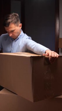 dikey video adam açık paket bandı ve bir kırmızı bant dağıtıcı ile kahverengi karton kutu mühürleme, diğer kutular ile taşınma, nakliye veya depolama için öğeler hazırlama arka planda