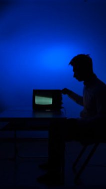 Dikey video. Eski bir eski televizyondan sinyal ayarlayan bir adamın silueti. Adam kanal değiştiriyor, eski televizyonun akort düğmelerini çeviriyor. Sinyal kaybı.