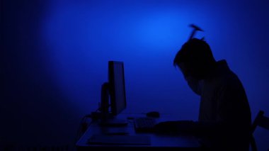 Masada oturan silüetli bir adam dramatik mavi ışık altında bilgisayar monitörünü öfkeyle kırıyor. Aşırı hayal kırıklığını ve sistem arızasını simgeliyor.