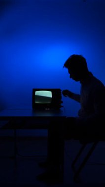 Dikey video. Eski bir eski televizyondan sinyal ayarlayan bir adamın silueti. Adam kanal değiştiriyor, eski televizyonun akort düğmelerini çeviriyor. Sinyal kaybı.