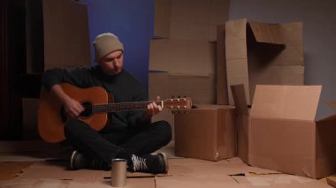 Karton çarşaflarda akustik gitar çalan bir adam bağış kutusuyla çevrili, sokak müzisyenleri şehir ortamında sokak çalgıcılığı yapıyor, mücadele ediyor ve umut veriyor.