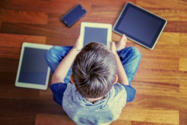 Küçük çocuk kullanarak tablet Pc ahşap yere oturma. Dijital tablet, dizüstü bilgisayar, cep telefonları her yerde. Seçici odak. Tonlu görüntü. Üstten Görünüm. Eğitim, öğrenme, teknoloji kavramı