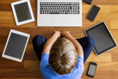 Küçük çocuk dizüstü bilgisayar kullanarak ahşap yere oturma. Dijital tablet, cep telefonları her yerde. Üstten Görünüm. Eğitim, öğrenme, teknoloji kavramı