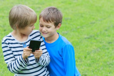 Çocuk cep telefonu ile. Gülümseyen, ekrana bakarak, oyun veya uygulama kullanarak iki erkek. Açık. Teknoloji eğitim eğlence insanlar dostluk kavramı