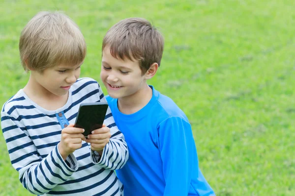Niños con smartphone. Dos chicos mirando a la pantalla, jugando juegos o utilizando la aplicación. Al aire libre. Tecnología educación ocio personas amistad concepto — Foto de Stock