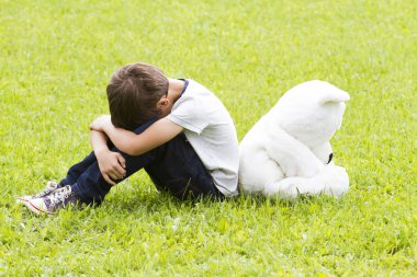 Bir oyuncak ayı ile oturan üzgün küçük çocuk. Her ikisi de çevirdim ve başlarını düşürdü. Üzüntü, korku, hayal kırıklığı, yalnızlık kavramı