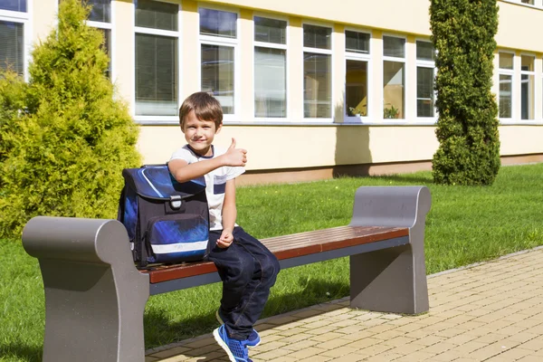 Liten pojke nära förskolan sitter på bänken. Barnet ler. Han mår mycket glada över att gå tillbaka till skolan. Utomhus — Stockfoto