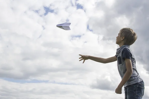 Chico volando un avión de papel contra el cielo azul — Foto de Stock